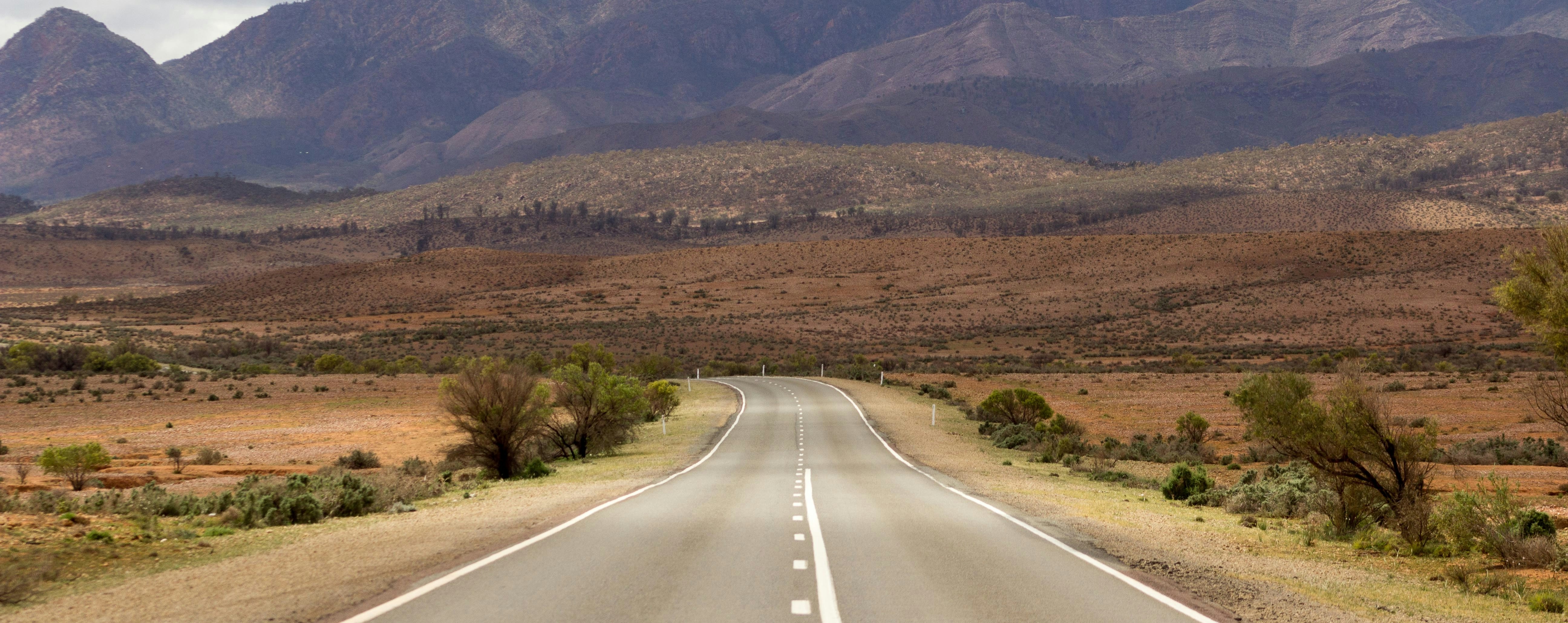 An empty outback highway running straight toward dry mountain ranges