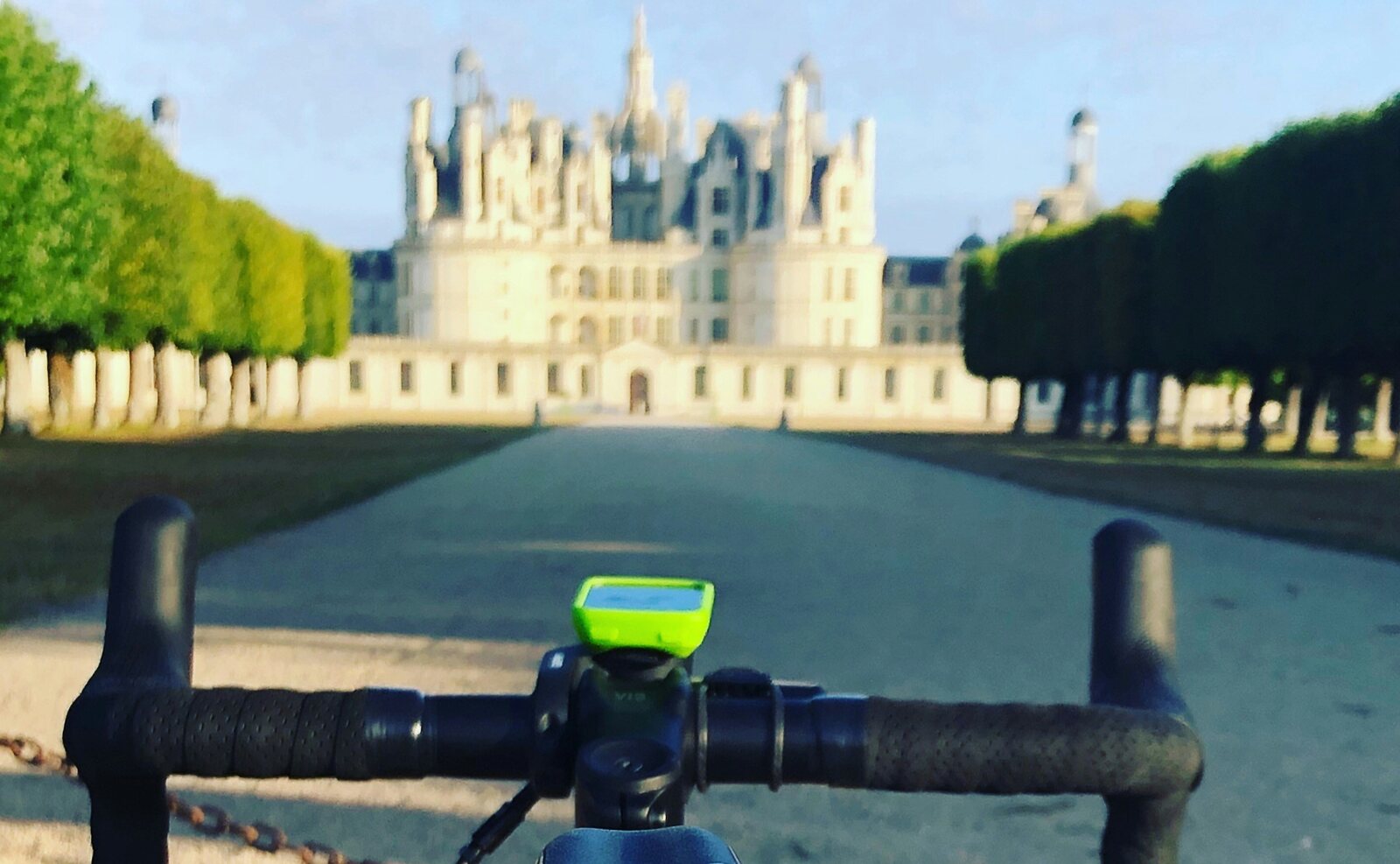 The best kind of detour - Château de Chambord at the end of the drive A road bike's cockpit looking down a tree-lined avenue towards the Château de Chambord
