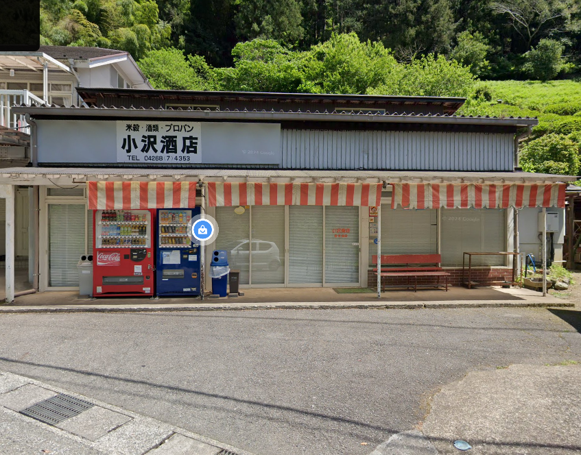 Red and blue vending machines under the striped awning of a rural sake shop with tea fields behind