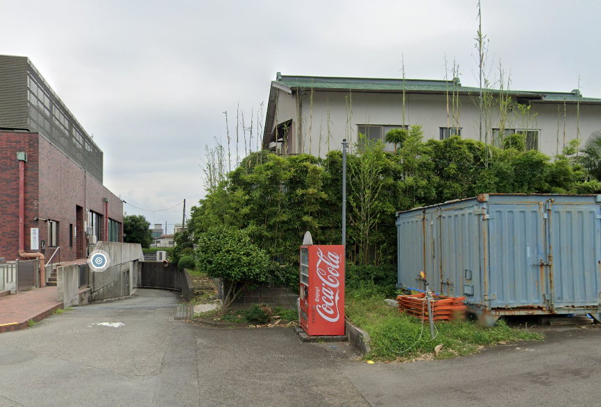 A lone red vending machine on a lane corner against a hedge in Susono