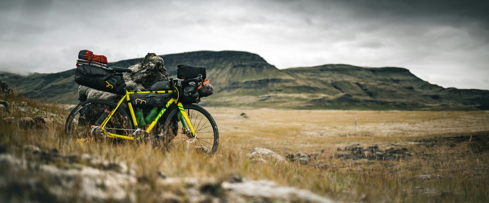 A fully loaded bikepacking bike leaning against a rock in open moorland under a stormy sky
