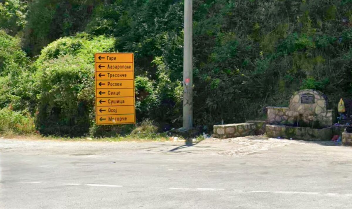 A stone fountain with a memorial plaque beside a junction signpost in Cyrillic script